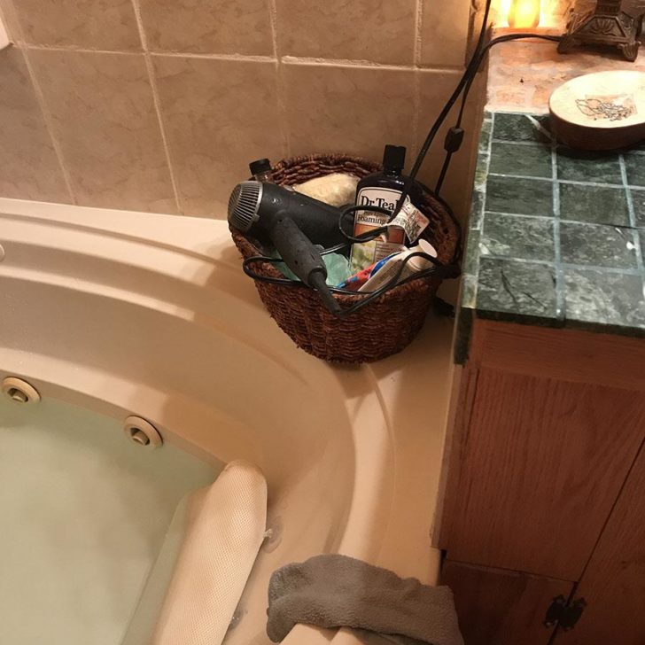 Plugged in hairdryer sitting on the edge of a full tub